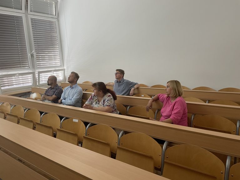 pet poslusalcev sedi za klopjo in gleda na na projekcijo